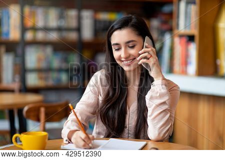 Job Hunting. Happy Arab Woman Talking By Smartphone With Hr Representetive And Taking Notes, Sitting