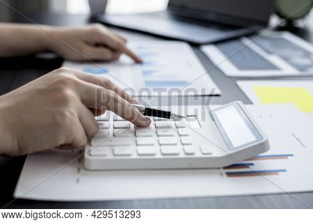 Close-up Of Woman Holding A Pen And Pressing A White Calculator, A Corporate Finance Auditor Examini