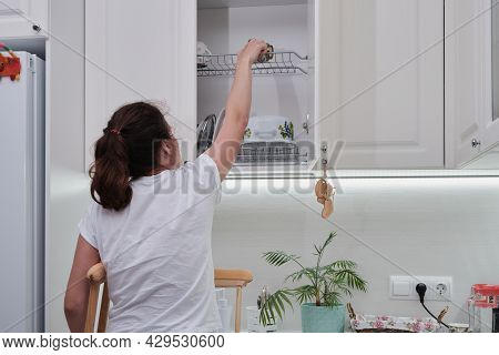 Woman On Crutches Washes The Dishes In The Kitchen. Temporary Limitation Of The Physical Capabilitie
