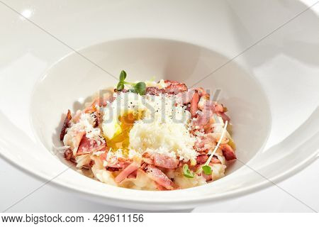 Risotto alla carbonara on white restaurant plate. Risotto with bacon and egg, garnished with micro greens. Risotto topped with parmesan cheese