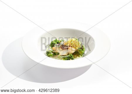 Panfried Fish with broccoli and cream sauce. Healthy roasted cod with green leaves. Fried Fish on white restaurant plate isolated on white background
