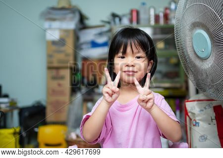 Cute Asian Child Girl Sweet Smile. Happy Kid Raise Finger In A V Shape, Raise Her Index And Middle F
