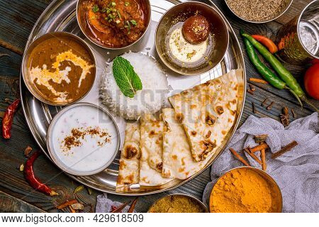 Assorted indian food set on wooden background. Dishes and appetisers of indeed cuisine, rice, lentils, paneer, samosa, spices, masala. Bowls and plates with indian food