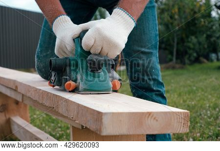 Carpenter Hands In Gloves Electric Plane Planing Lumber, Flying Shavings, Sawdust. Close-up On Glove