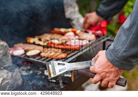 Man Cooking Meat On Barbecue Grill At Bbq Party