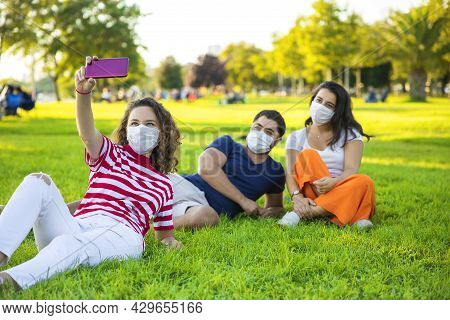 Friends With A Protective Masks Sitting On The Grass And Taking A Selfie