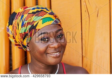 African Woman With A Hopeful Happy Smile And Traditional Headdress Standing Against A Painted Wooden