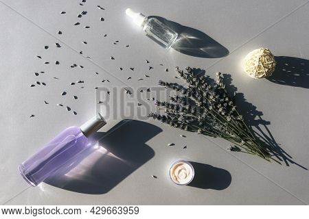Lavender Flowers And Hydrolat, Serum In Glass Bottles, Cream Jar On Light Gray Background, Top View.