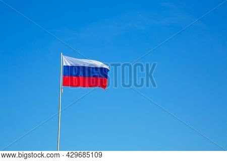 Russian Flag On A Pole Against Blue Sky. Copy Space