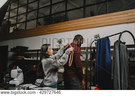 Corean Female Tailor Measuring Black Man In Workshop