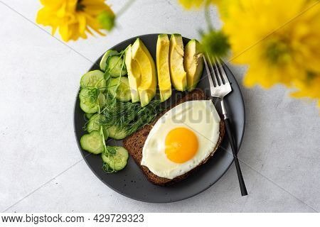 Delicious Breakfast With Avocado, Fresh Cucumbers And Microgreens Of Peas With Dill, Fried Eggs On B
