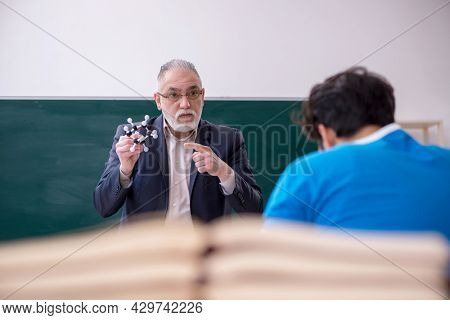 Old male physics teacher and young male student in front of blac
