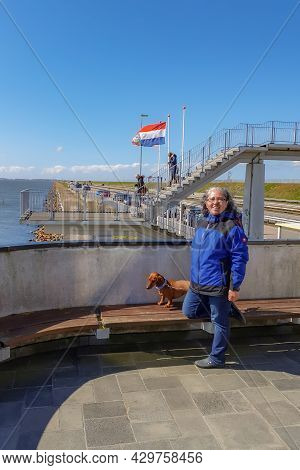 Ijsselmeer In The Netherlands. 17 April 2021. Mature Woman With Her Brown Short Haired Dachshund Sta