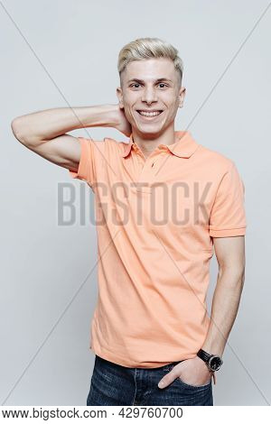 Portrait Of A Smiling Blonde Man Standing In Front Of A Gray Background With Hand In His Hair
