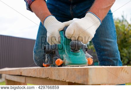 Carpenter Hands In Gloves Electric Plane Planing Lumber, Flying Shavings, Sawdust. Close-up On Glove