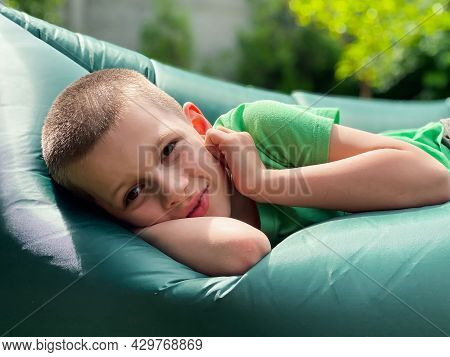 Portrait Of A Caucasian Boy 7 Years Old In A Green T-shirt Resting On A Lamzak, Inflatable Lounger.