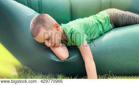 Portrait Of A Caucasian Boy 7 Years Old In A Green T-shirt Resting On A Lamzak, Inflatable Lounger.