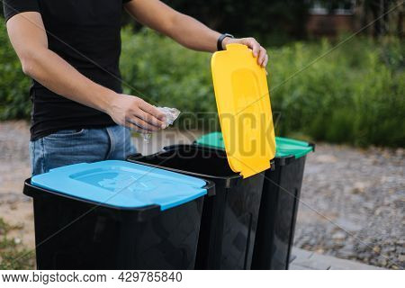 Man Throwing Plastic Bag Into Recycling Bin On Back Yard. Close Up Of Humen Hand Hold Rubbish. Diffe