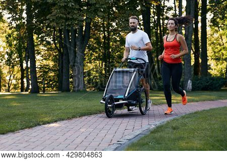 Family With Child Runs With A Jogging Stroller Through A City Park