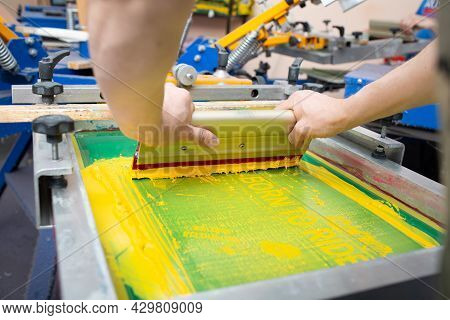 Serigraphy Silk Screen Print Process At Clothes Factory. Frame, Squeegee And Plastisol Color Paints.