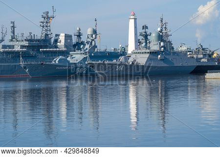 Kronstadt, Russia - August 11, 2021: Ancient Lighthouse Among The Warships Of The Baltic Fleet On A 