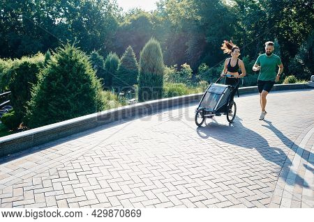 Family With Child Runs With A Jogging Stroller Through A City Park