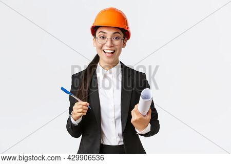 Smiling Professional Female Architect, Asian Engineer In Helmet And Business Suit, Holding Blueprint