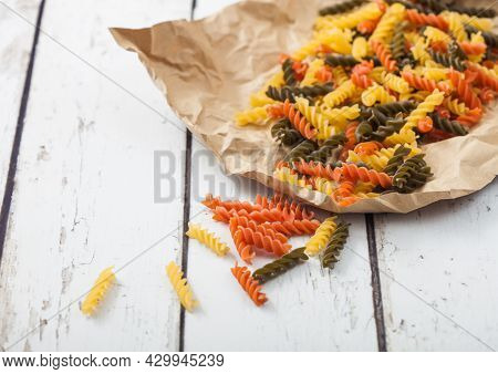 Raw Homemade Tricolore Fusilli Pasta In Brown Paper On White Wooden Table Background.