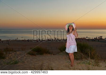 Woman In A White Dress On A Background Of The Sea At Sunset.