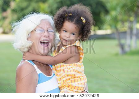 Portrait of a caucasian grandma carrying her little hispanic granddaughter and laughing