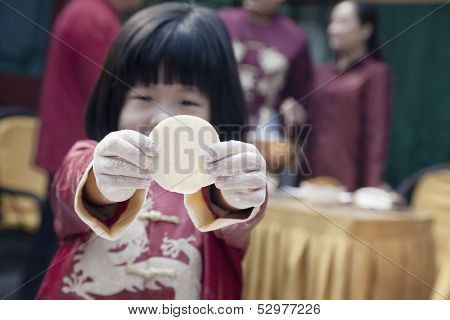 Little girl showing dumpling wrapper in traditional clothing
