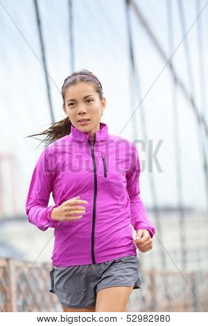 Running woman jogging and training in city. Female runner in the rain outside. Multiracial Asian Caucasian woman fitness sport model sprinting on Brooklyn Bridge, New York City, USA.