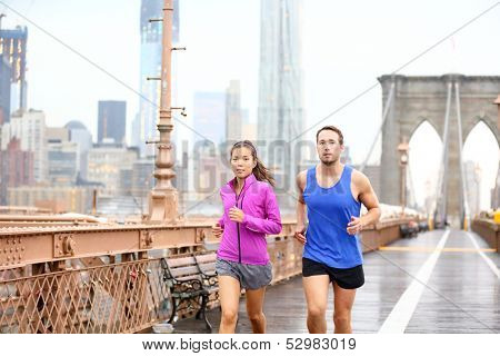 Esecuzione di coppia. Corridori jogging fuori nella pioggia. Donna asiatica e caucasica uomo fitness e runner sp