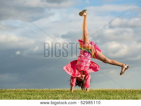 The little girl turns like a wheel on the grass on a background of sky and clouds