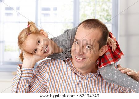 Little daughter around father's neck having fun, both laughing.