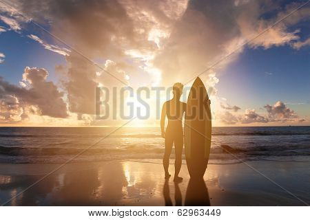 Surfing Man Standing On A Beach With Sunset Background