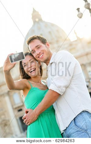 Tourists couple selfie by Vatican city and St. Peter's Basilica church in Rome. Happy travel woman and man taking selfie photo picture on romantic honeymoon in Italy.