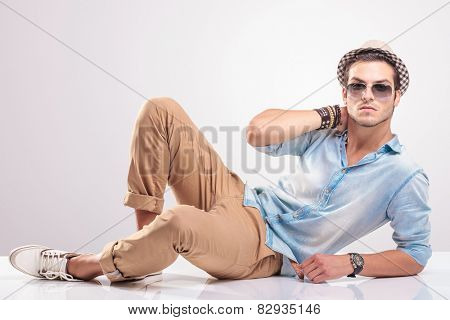 Young fashion man holding his hand to his neck while lying on the floor.