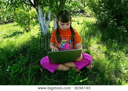 Mädchen mit einem Laptop unter dem Baum
