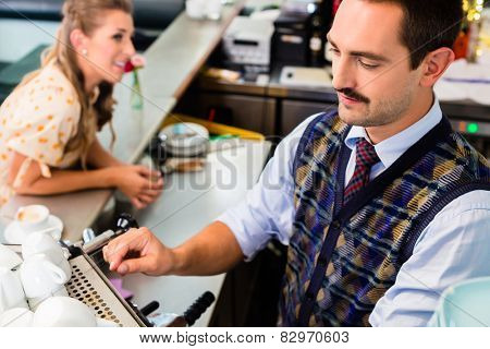 Girl in cafe or coffee bar flirting with barista who is busy preparing Cappuccino with professional machine
