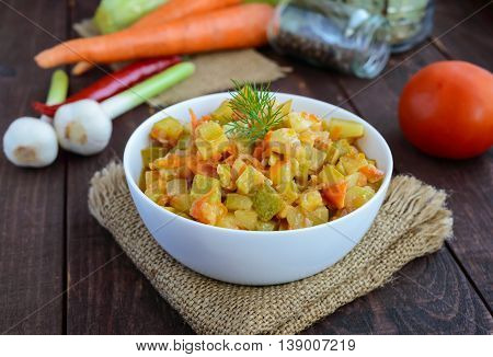 Vegetarian ragout of summer vegetables (zucchini carrots tomatoes spices garlic chilli) in a white bowl on a wooden background. Dietary dish.