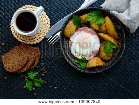 Fried egg in salami and baked potatoes. Submission of a frying pan with a cup of coffee and rye bread. Breakfast. The top view