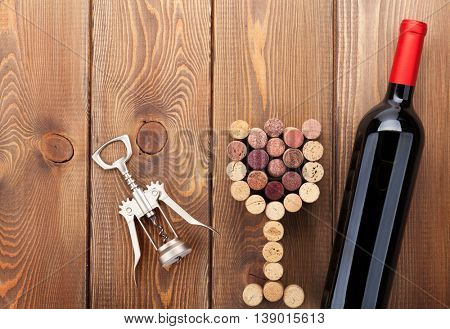 Red wine bottle, glass shaped corks and corkscrew. View from above over rustic wooden table background