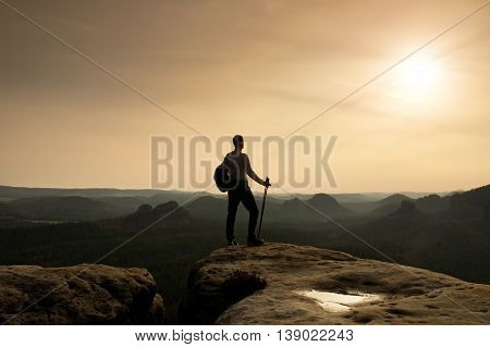 Tourist On Cliff Edge With Pole In Hand And Backpack
