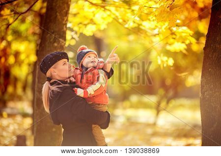 Beautiful baby boy and mother in autumn garden