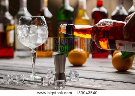 Bottle pours liquid into jigger. Ice cubes in wineglass. Dry wine for tasty cocktail. Key ingredient for alcoholic beverage.
