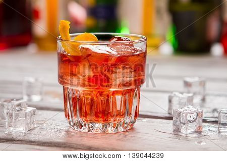 Dark orange drink in glass. Ice cubes and lemon peel. Negroni served at local bar. Vermouth and gin.