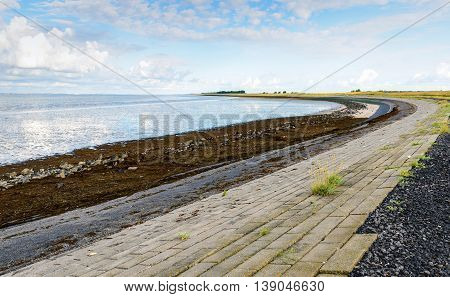 Curved embankment next to a Dutch estuary at low tide on an early morning in the summer season.