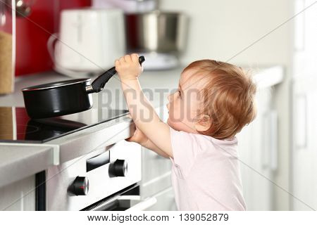 Little child playing with pan and electric stove in the kitchen