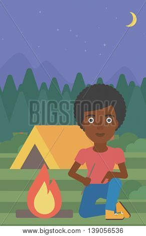 An african-american woman kindling campfire on the background of camping site with tent. Tourist relaxing near campfire. Woman sitting near campfire. Vector flat design illustration. Vertical layout.